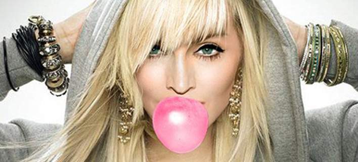 Η Madonna με γκρι φούτερ και ξανθά μαλλιά κάνει φούσκα με τσίχλα.