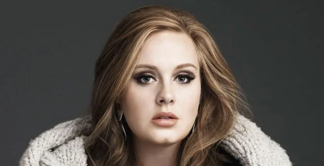 Πορτρέτο της Adele με ξανθά μαλλιά και γκρι πλεκτή ζακέτα.