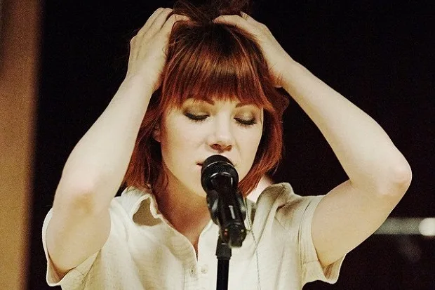 Η Carly Rae Jepsen τραγουδάει σε μικρόφωνο με τα χέρια στα μαλλιά της.