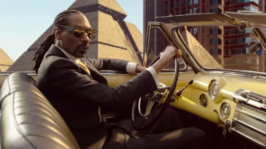 Ο Snoop Dogg οδηγεί ένα κλασικό κίτρινο αυτοκίνητο με φόντο πυραμίδες.