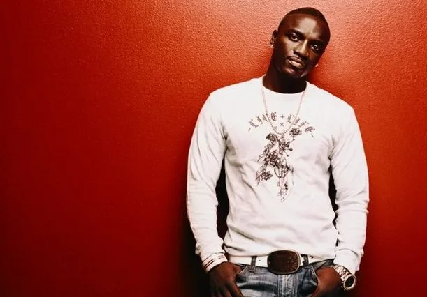 Ο Akon ποζάρει μπροστά από έναν κόκκινο τοίχο.