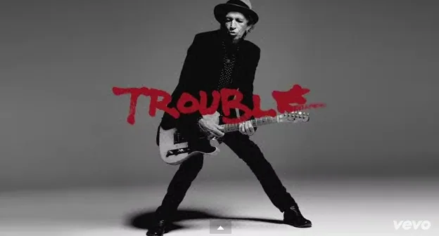 Ο Keith Richards παίζει κιθάρα σε ασπρόμαυρο φόντο με την επιγραφή Trouble.