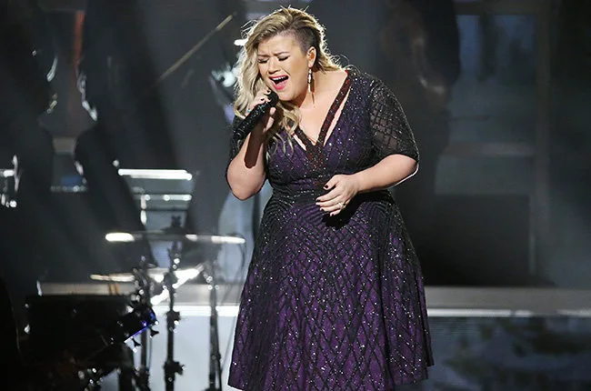 Η Kelly Clarkson τραγουδάει στη σκηνή κρατώντας μικρόφωνο.