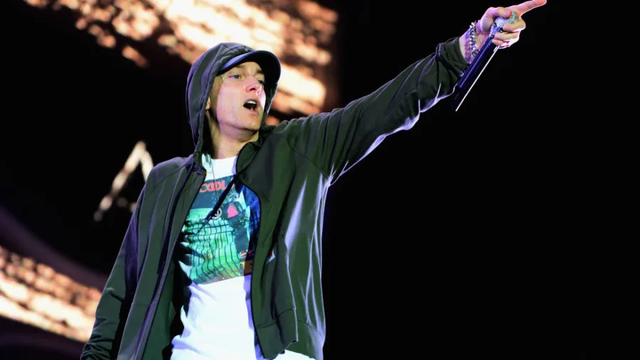 Ο Eminem στη σκηνή με γκρι φούτερ και καπέλο, κρατώντας μικρόφωνο.