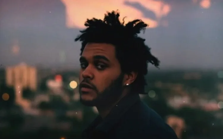Ο The Weeknd σε εξωτερικό χώρο με φόντο το ηλιοβασίλεμα και την πόλη.