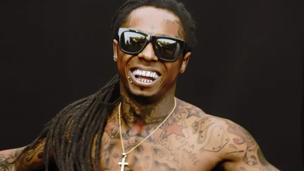 Ο Lil Wayne χαμογελάει φορώντας γυαλιά ηλίου και δείχνοντας τα τατουάζ του.