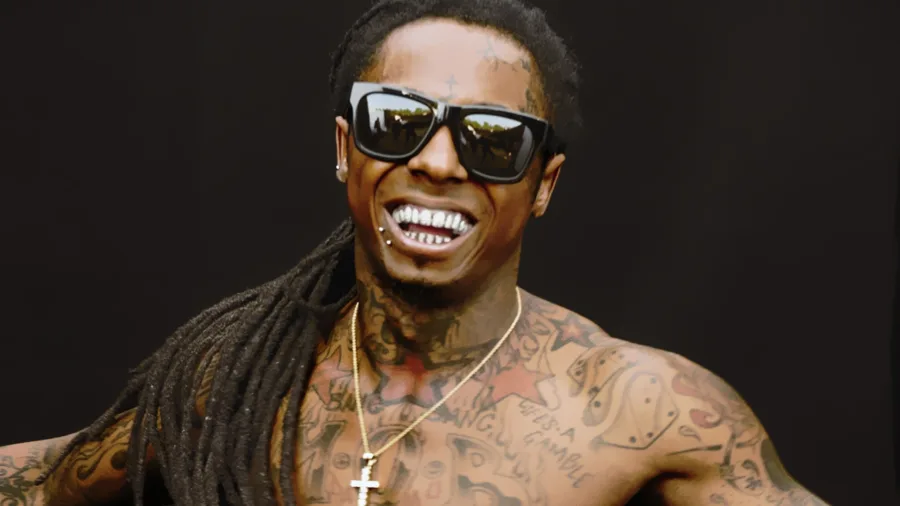 Ο Lil Wayne χαμογελάει φορώντας γυαλιά ηλίου και δείχνοντας τα τατουάζ του.
