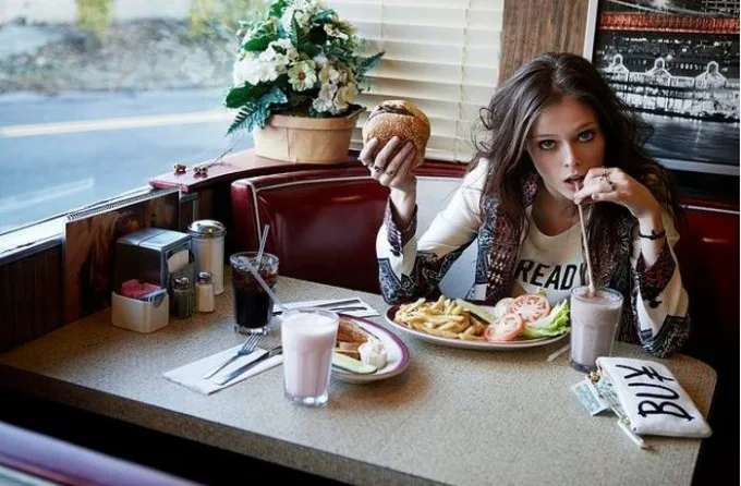 Κοπέλα σε αμερικάνικο diner τρώει burger και πίνει milkshake.