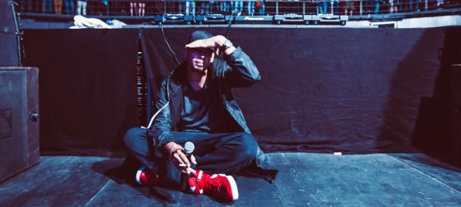 Ο Afrojack κάθεται στη σκηνή φορώντας κόκκινα αθλητικά παπούτσια.
