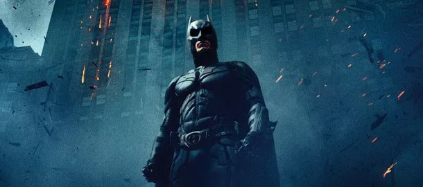 Ο Batman στέκεται μπροστά από ένα κτίριο που καταρρέει.