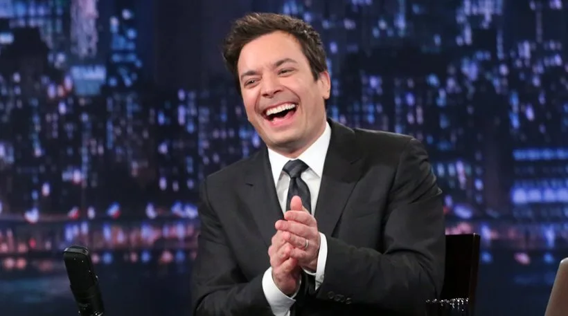 Ο Jimmy Fallon γελάει και χειροκροτά στο πλατό του The Tonight Show.
