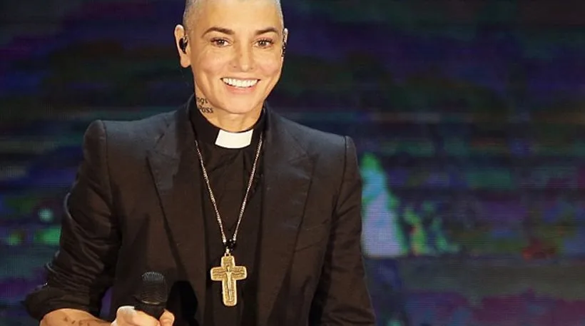 Η Sinead O’Connor σε σκηνή με ιερατικό κολάρο και σταυρό.