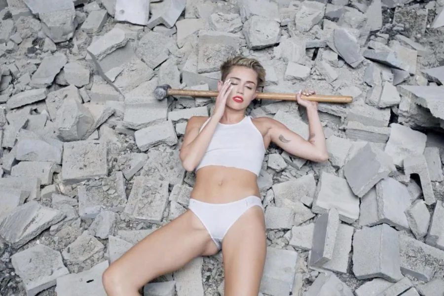 Η Miley Cyrus ξαπλωμένη σε συντρίμμια κρατώντας μια βαριοπούλα.