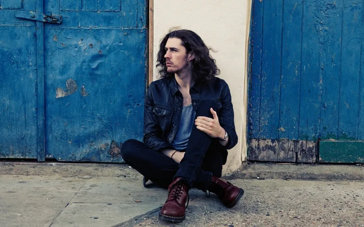 Ο Hozier κάθεται στο έδαφος μπροστά από μπλε ξύλινες πόρτες.