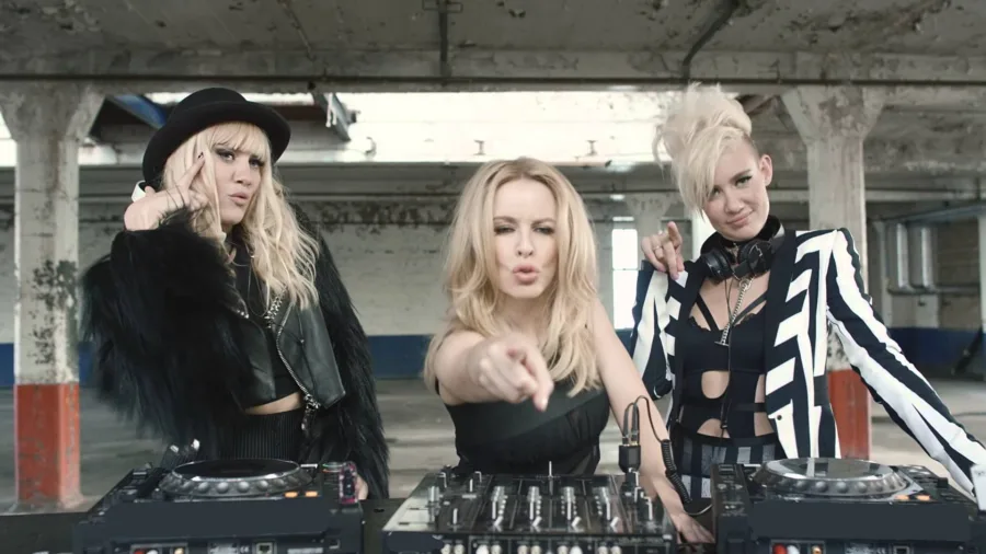 Οι NERVO και η Kylie Minogue σε σκηνικό βιομηχανικού χώρου με DJ decks.