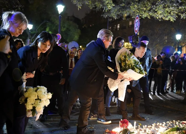 Irish band U2 lead singer Bono (C) and drummer Larry Mullen Jr (R) pay homage to attacks' victims near the Bataclan concert hall on November 14, 2015 in Paris, a day after a series of coordinated attacks in and around Paris. Islamic State jihadists claimed a series of coordinated attacks by gunmen and suicide bombers in Paris that killed at least 129 people in scenes of carnage at a concert hall, restaurants and the national stadium. U2 has canceled two sold-out concerts in Paris, including one to be broadcast live on November 14, and Foo Fighters cut short their tour after attacks that killed at least129 people. AFP PHOTO / FRANCK FIFE