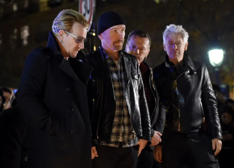 Irish band U2 (From L) lead singer Bono, guitarist The Edge, drummer Larry Mullen Jr and bass player Adam Clayton pay homage to attacks victims near the Bataclan concert hall on November 14, 2015 in Paris, a day after a series of coordinated attacks in and around Paris. Islamic State jihadists claimed a series of coordinated attacks by gunmen and suicide bombers in Paris that killed at least 129 people in scenes of carnage at a concert hall, restaurants and the national stadium. U2 has canceled two sold-out concerts in Paris, including one to be broadcast live on November 14, and Foo Fighters cut short their tour after attacks that killed at least129 people. AFP PHOTO / FRANCK FIFE