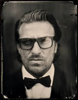 Ο Parov Stelar σε ασπρόμαυρο πορτρέτο με γυαλιά και παπιγιόν.