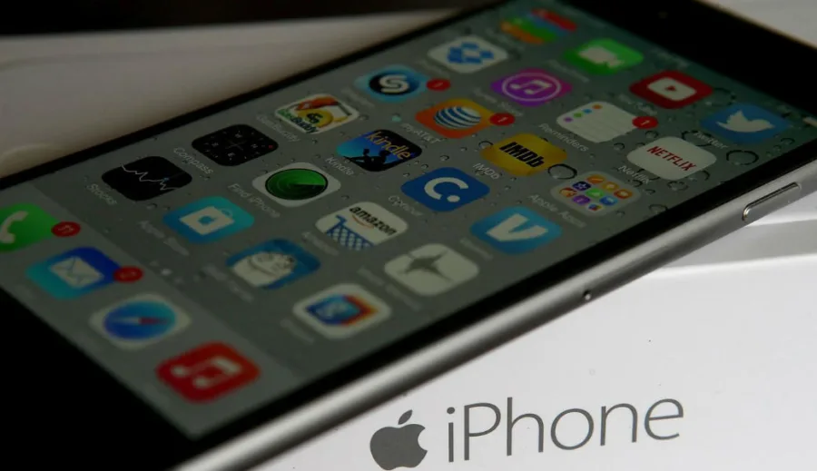 Κοντινό πλάνο ενός Apple iPhone με εικονίδια εφαρμογών στην οθόνη και τη συσκευασία του.