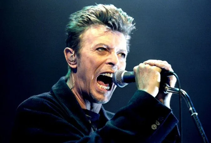 Ο David Bowie τραγουδάει σε μικρόφωνο κατά τη διάρκεια συναυλίας.