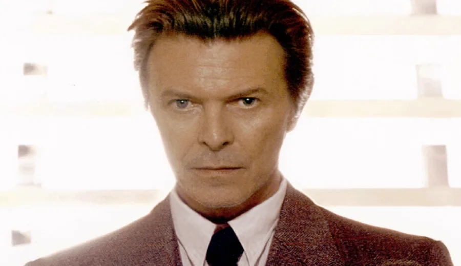 Ο David Bowie με κοστούμι και γραβάτα σε φωτεινό φόντο.