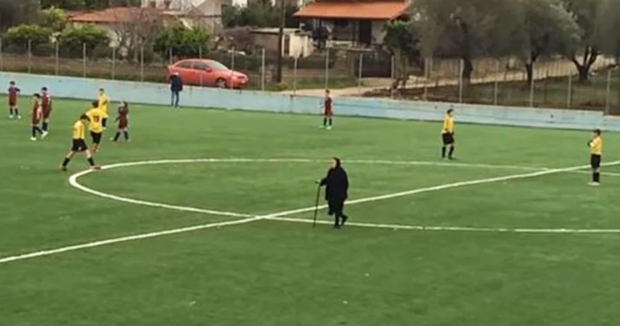 Μια γιαγιά με μπαστούνι διασχίζει το κέντρο ενός γηπέδου ποδοσφαίρου κατά τη διάρκεια αγώνα.