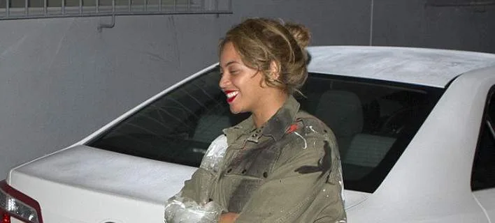 Η Beyonce με messy bun και κόκκινο κραγιόν δίπλα σε λευκό αυτοκίνητο.