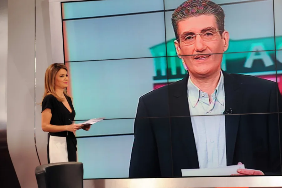 Παρουσιάστρια ειδήσεων σε στούντιο της ΕΡΤ1 με φόντο μεγάλη οθόνη.