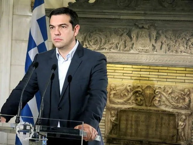 Ο Αλέξης Τσίπρας σε ομιλία πίσω από πόντιουμ με την ελληνική σημαία.