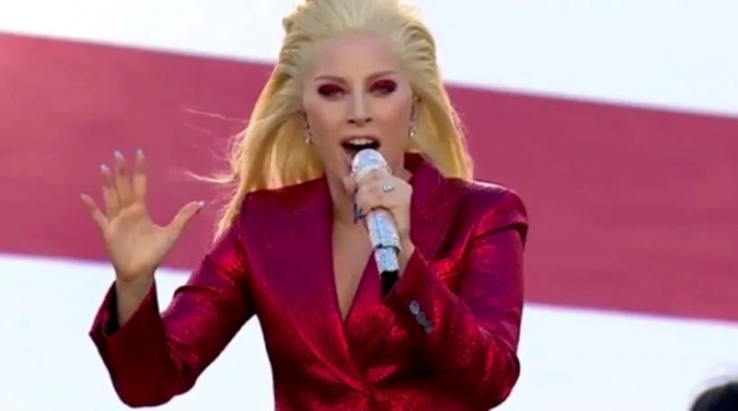Η Lady Gaga τραγουδάει με κόκκινο κοστούμι και ασημένιο μικρόφωνο.