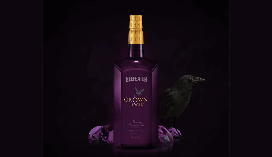 Μπουκάλι Beefeater Crown Jewel gin σε μωβ φόντο με ένα κοράκι και πολύτιμους λίθους.
