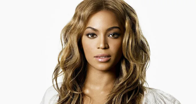 Κοντινό πορτρέτο της Beyoncé με κυματιστά μαλλιά σε λευκό φόντο.