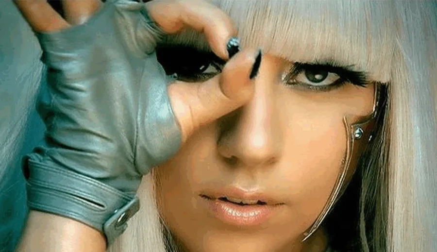 Κοντινό πλάνο της Lady Gaga με ξανθά μαλλιά, γκρι γάντι και έντονο μακιγιάζ.