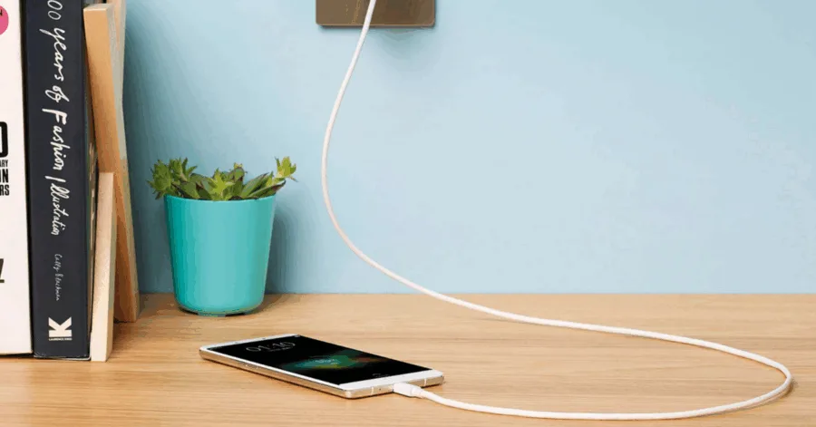 Κινητό τηλέφωνο OPPO που φορτίζει πάνω σε ξύλινο γραφείο δίπλα σε γλάστρα και βιβλία.