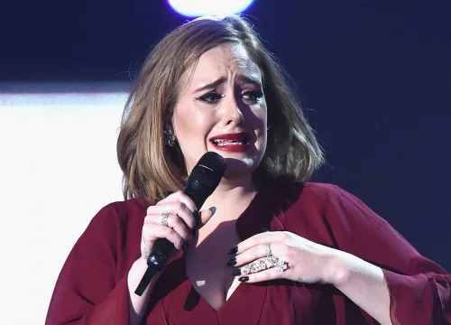 Η Adele συγκινημένη στη σκηνή κρατώντας μικρόφωνο.