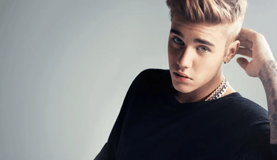 Ο Justin Bieber ποζάρει με μαύρη μπλούζα και το χέρι στο κεφάλι.