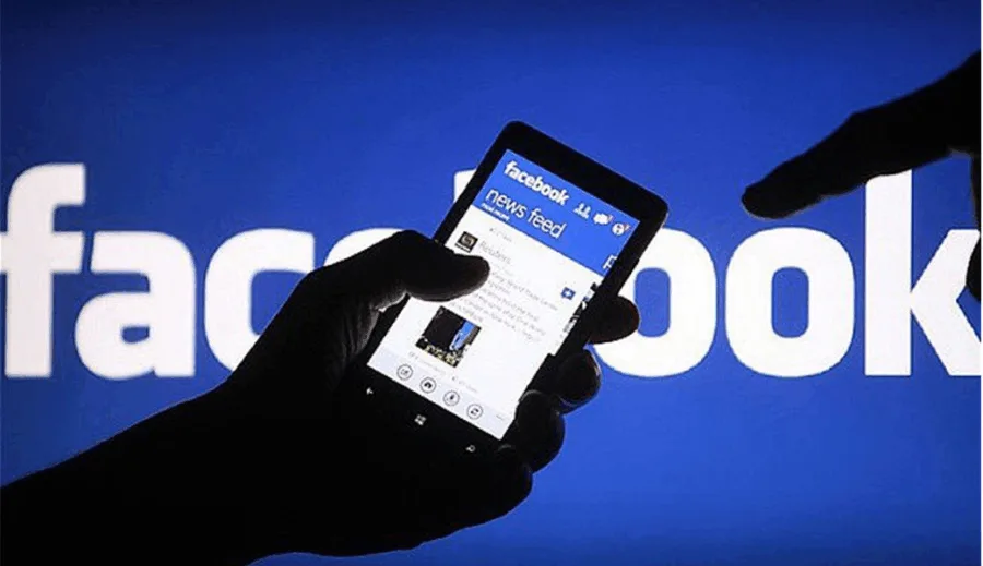 Χέρια που κρατούν smartphone με την εφαρμογή Facebook μπροστά από το λογότυπο της εταιρείας.