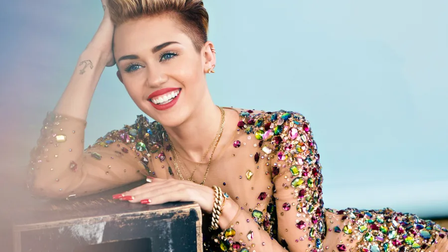 Η Miley Cyrus με κοντό ξανθό μαλλί και φόρεμα με πολύχρωμες πέτρες.