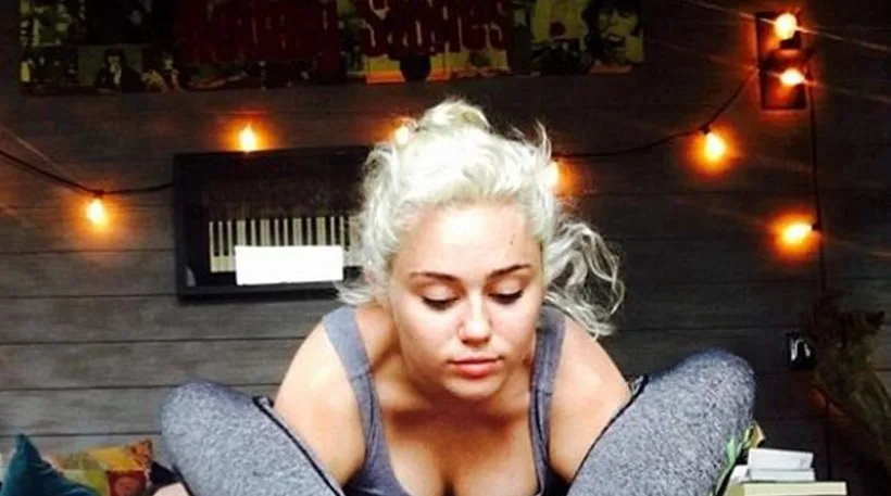 Η Miley Cyrus κάνει γιόγκα σε εσωτερικό χώρο με ατμοσφαιρικό φωτισμό.