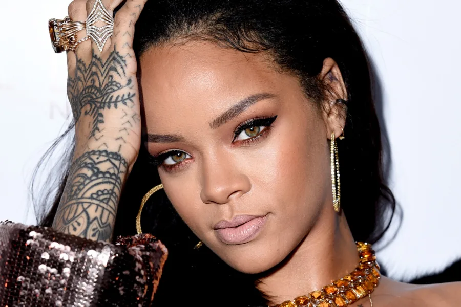 Κοντινό πορτρέτο της Rihanna με έντονο μακιγιάζ στα μάτια και τατουάζ στο χέρι.