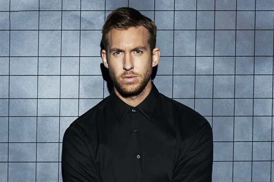 Ο Calvin Harris με μαύρο πουκάμισο μπροστά από γκρίζο τοίχο με τετράγωνα.