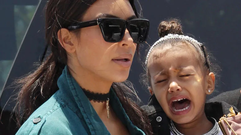 Η Kim Kardashian με μαύρα γυαλιά ηλίου δίπλα στην κόρη της που κλαίει.