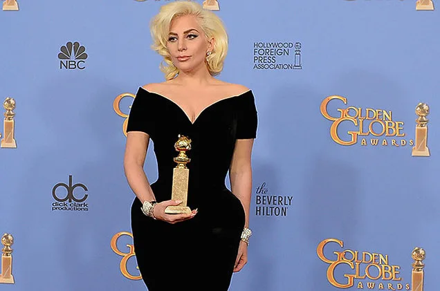 Η Lady Gaga με μαύρο φόρεμα κρατάει ένα βραβείο Golden Globe.