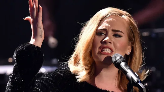 Η Adele τραγουδάει με πάθος σε συναυλία κρατώντας το μικρόφωνο.