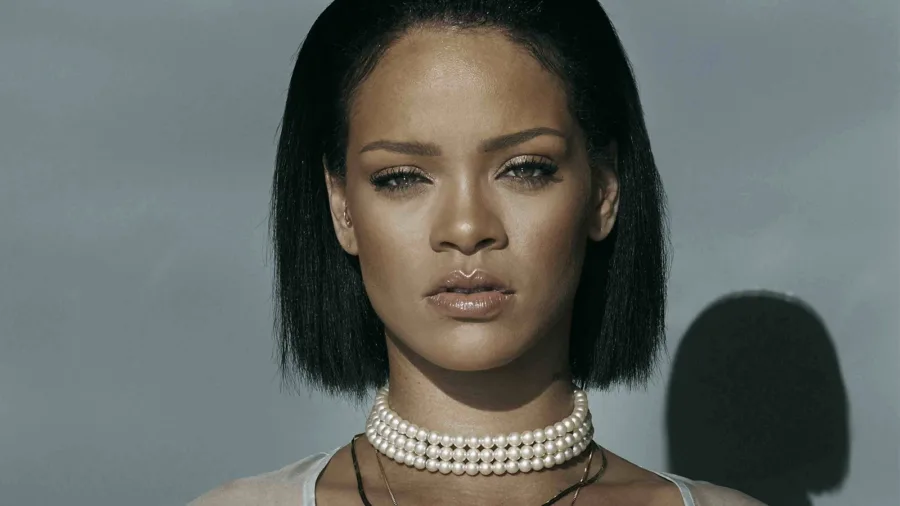 Κοντινό πορτρέτο της Rihanna με κοντό μαύρο καρέ μαλλί και πέρλες στο λαιμό.