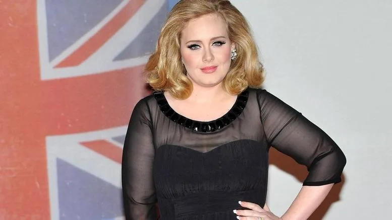 Η Adele σε επίσημη εμφάνιση με μαύρο φόρεμα μπροστά από τη βρετανική σημαία.