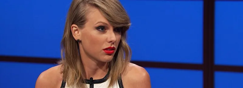 Η Taylor Swift με ξανθά μαλλιά και κόκκινο κραγιόν σε μπλε φόντο.