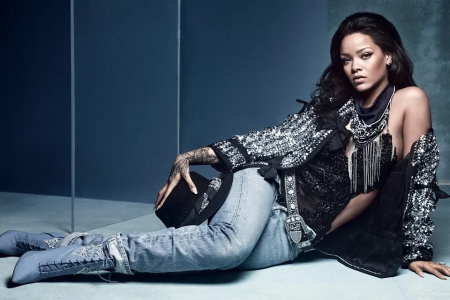 Η Rihanna ποζάρει ξαπλωμένη με τζιν παντελόνι και λαμπερό σακάκι.