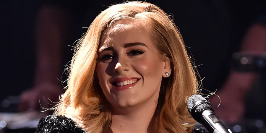 Η Adele χαμογελάει σε σκηνή κρατώντας μικρόφωνο.