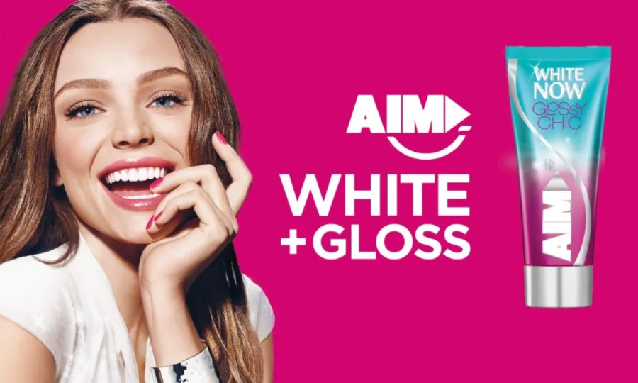 Διαφημιστική εικόνα της οδοντόκρεμας AIM White Now Glossy Chic με χαμογελαστή γυναίκα.